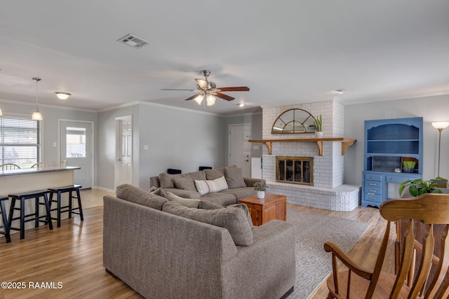 living area featuring light wood-style floors, ornamental molding, a ceiling fan, and visible vents