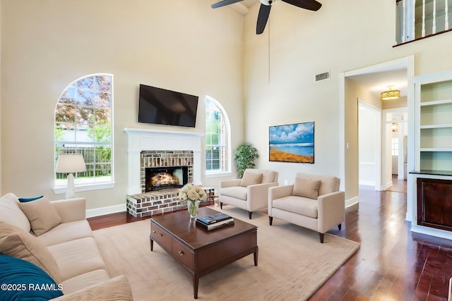 living room featuring a towering ceiling, a ceiling fan, wood finished floors, and visible vents