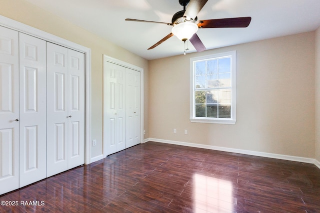 unfurnished bedroom with two closets, baseboards, a ceiling fan, and wood finished floors