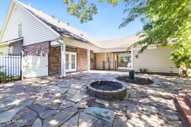 rear view of house with french doors, fence, brick siding, a patio, and an outdoor fire pit