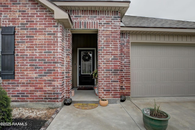 view of exterior entry with an attached garage and brick siding