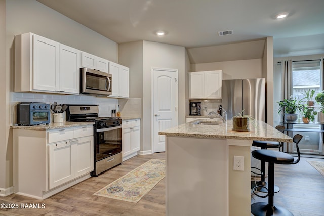 kitchen with light wood finished floors, stainless steel appliances, a kitchen breakfast bar, a sink, and visible vents