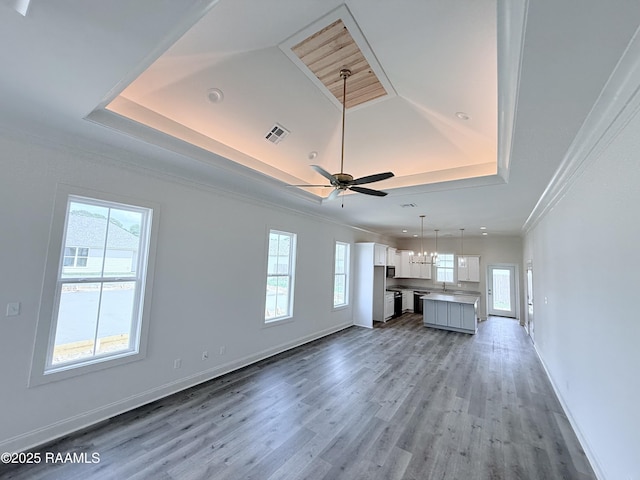 219 Berchman Oaks Dr, Lafayette, LA 70506 - unfurnished living room featuring a tray ceiling, ornamental molding, plenty of natural light, light wood-type flooring, and baseboards