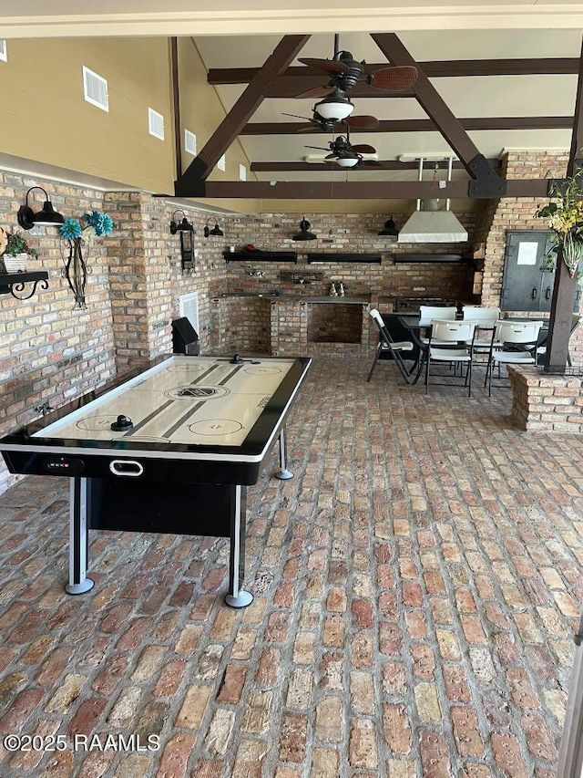 rec room with brick floor, visible vents, a ceiling fan, and brick wall
