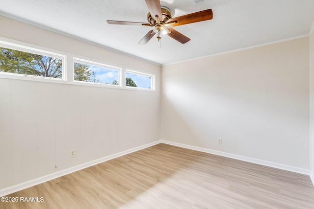 unfurnished room with light wood-type flooring, a ceiling fan, baseboards, and crown molding