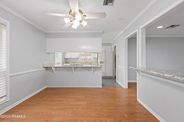kitchen featuring white fridge with ice dispenser, ceiling fan, a breakfast bar, white cabinetry, and a peninsula