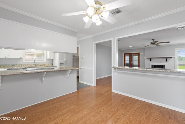 kitchen featuring white refrigerator with ice dispenser, a ceiling fan, a breakfast bar, white cabinetry, and light wood-type flooring