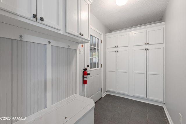 mudroom featuring dark tile patterned floors, a textured ceiling, and baseboards