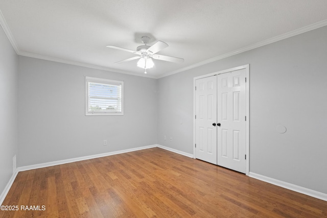 unfurnished bedroom featuring baseboards, wood finished floors, crown molding, a closet, and a ceiling fan