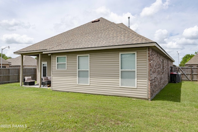 rear view of house with roof with shingles, brick siding, a fenced backyard, a patio area, and a yard