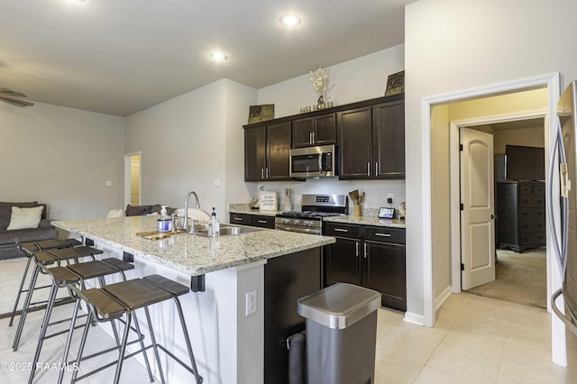 kitchen featuring a kitchen island with sink, a sink, light stone counters, a breakfast bar, and stainless steel appliances