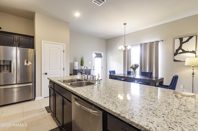 kitchen with appliances with stainless steel finishes, light stone counters, a sink, a chandelier, and light tile patterned floors