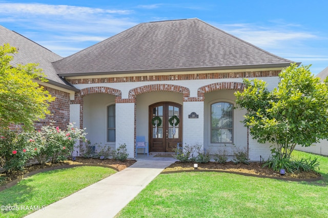 view of front of home featuring brick siding, french doors, a shingled roof, and a front yard