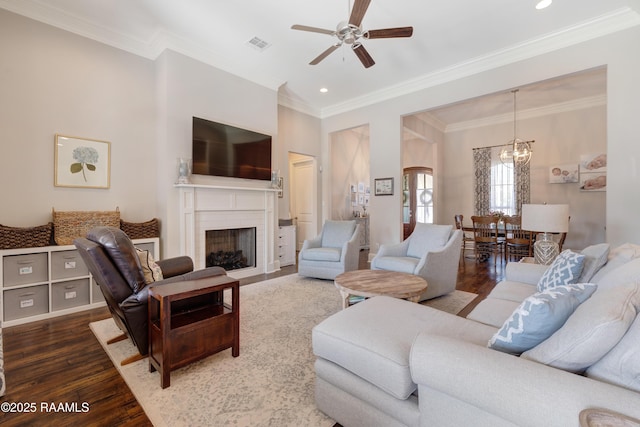living room featuring ceiling fan with notable chandelier, wood finished floors, visible vents, and crown molding