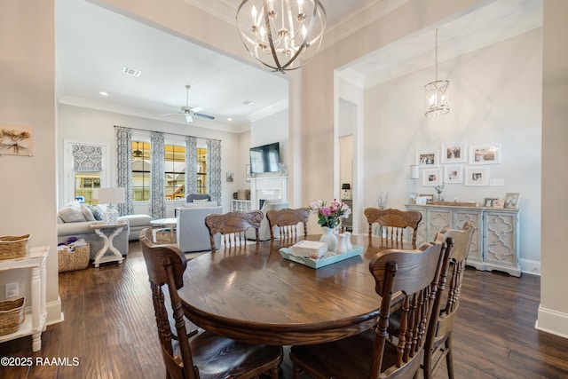 dining space featuring dark wood-style floors, visible vents, ceiling fan with notable chandelier, a fireplace, and ornamental molding