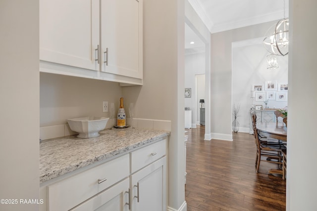 kitchen with white cabinets, light stone countertops, crown molding, dark wood-style flooring, and a notable chandelier