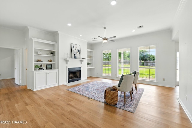 living room with a ceiling fan, ornamental molding, recessed lighting, a fireplace with flush hearth, and light wood-style flooring