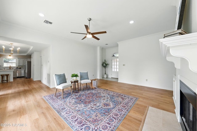 sitting room with crown molding, ceiling fan, visible vents, and a fireplace with flush hearth