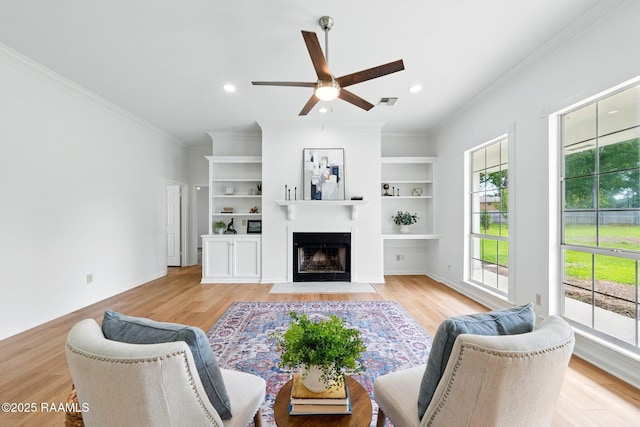 living area featuring crown molding, a ceiling fan, light wood-style flooring, and a fireplace with flush hearth