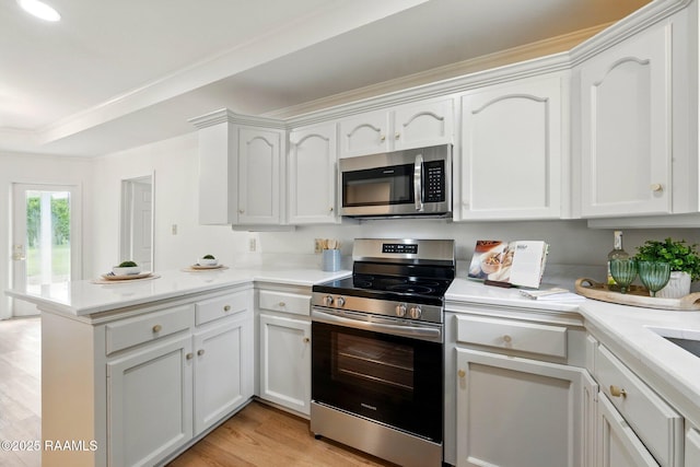 kitchen featuring appliances with stainless steel finishes, light countertops, white cabinets, a peninsula, and light wood-style floors