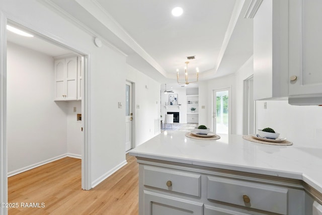 kitchen with light countertops, a peninsula, a raised ceiling, and light wood-type flooring