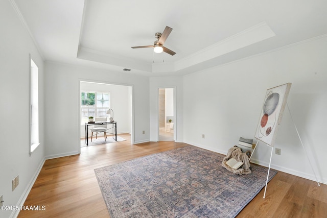 interior space featuring crown molding, baseboards, light wood-style flooring, and a raised ceiling