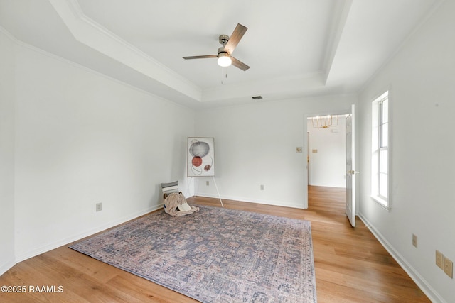 interior space featuring crown molding, light wood finished floors, a raised ceiling, and ceiling fan with notable chandelier