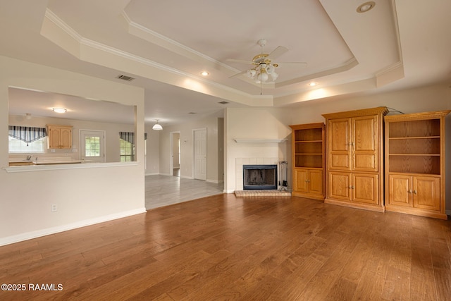 unfurnished living room with visible vents, ceiling fan, wood finished floors, and a raised ceiling