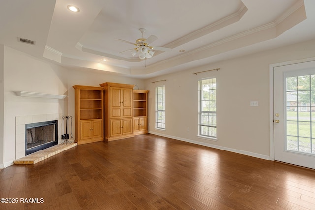 unfurnished living room featuring a tile fireplace, ceiling fan, a raised ceiling, visible vents, and ornamental molding