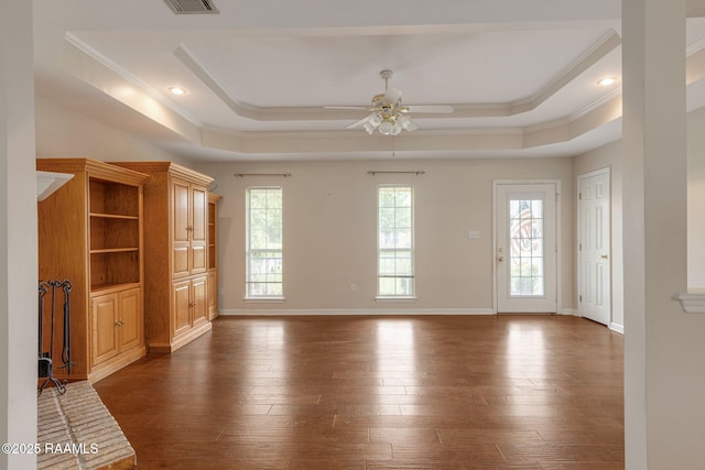 unfurnished living room featuring ceiling fan, a raised ceiling, baseboards, ornamental molding, and dark wood finished floors