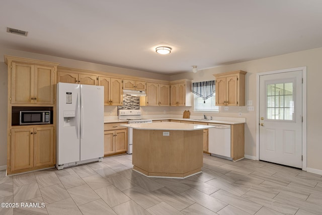 kitchen with white appliances, under cabinet range hood, light countertops, a center island, and visible vents