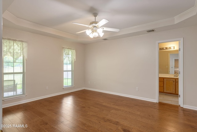 unfurnished room with light wood-type flooring, a raised ceiling, a ceiling fan, and a sink