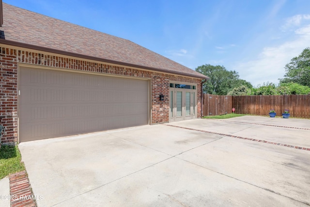 view of side of property featuring french doors, fence, concrete driveway, and brick siding