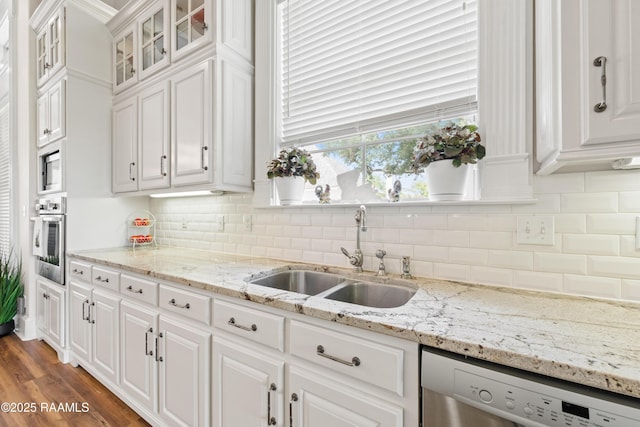 kitchen with white cabinets, appliances with stainless steel finishes, a sink, tasteful backsplash, and glass insert cabinets