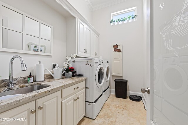 clothes washing area featuring crown molding, baseboards, washing machine and clothes dryer, a sink, and cabinet space