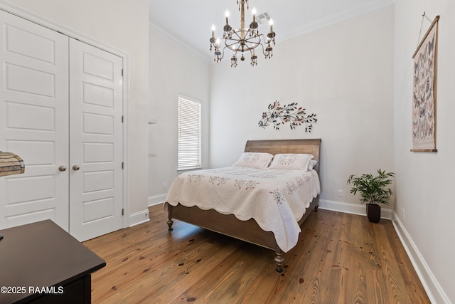 bedroom with a chandelier, baseboards, wood finished floors, ornamental molding, and a closet