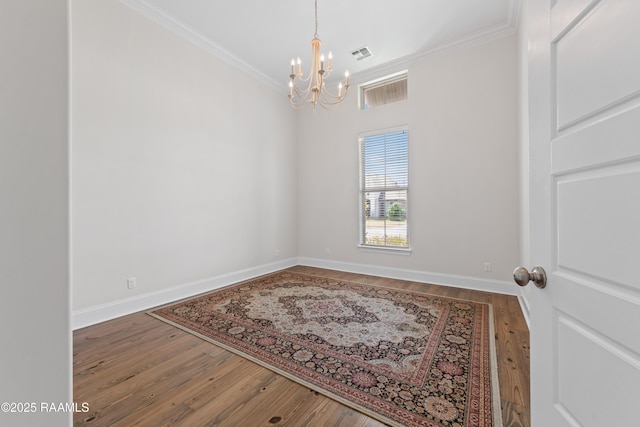 empty room featuring crown molding, a notable chandelier, baseboards, wood finished floors, and visible vents