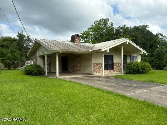 1614 Norway St, Opelousas, LA 70570 - view of front of house featuring a chimney, driveway, a front yard, metal roof, and a carport