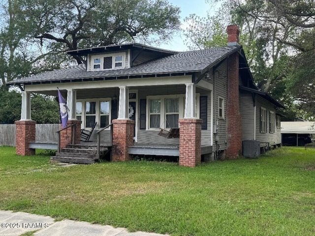 view of front of home featuring covered porch, a chimney, a front yard, central air condition unit, and a shingled roof