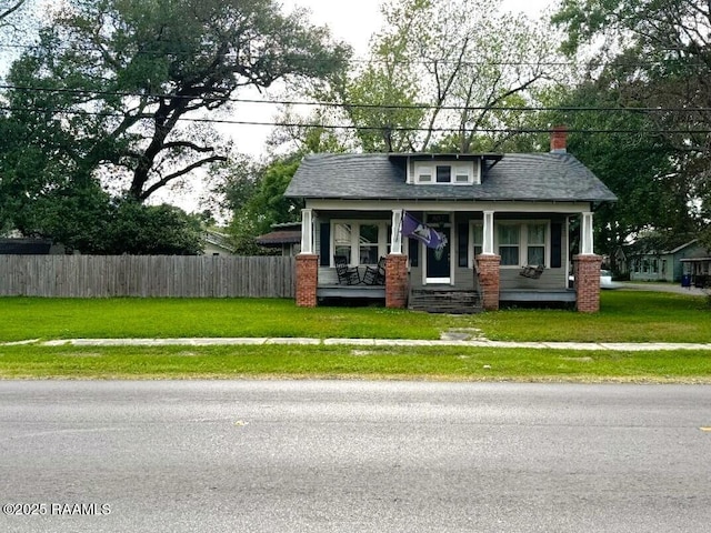 bungalow featuring fence, covered porch, a chimney, and a front lawn