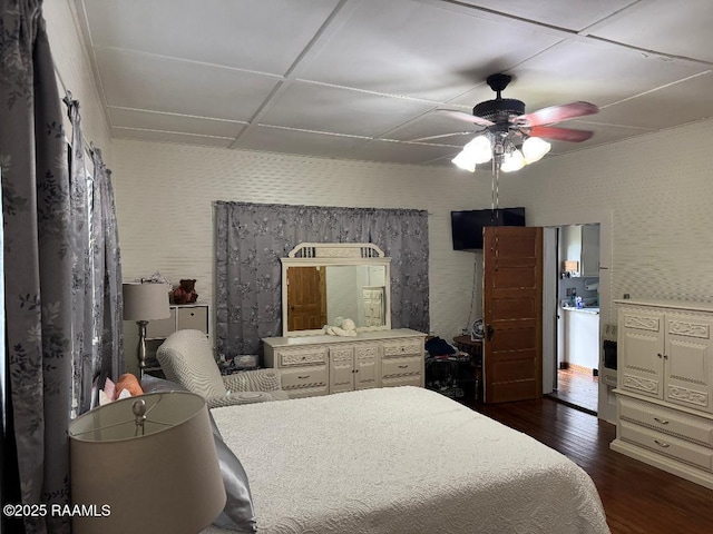 bedroom with a ceiling fan, wallpapered walls, and dark wood-style floors