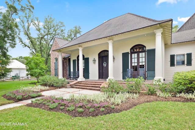 greek revival inspired property with a porch, roof with shingles, brick siding, and a front lawn