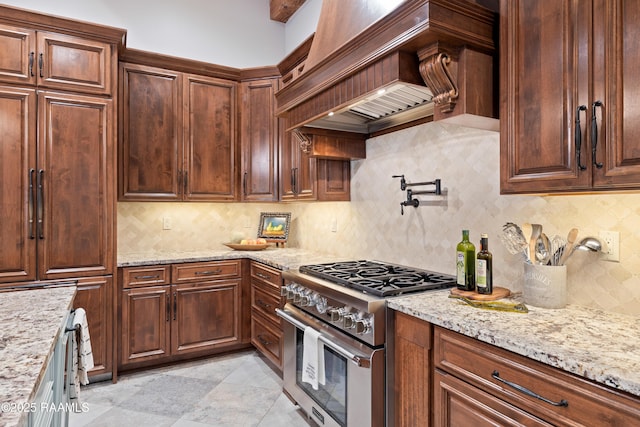 kitchen featuring high end stove, premium range hood, decorative backsplash, and light stone counters