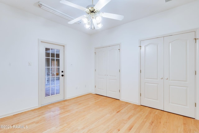 unfurnished bedroom featuring two closets, ceiling fan, wood finished floors, and baseboards