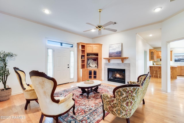 living room with recessed lighting, a warm lit fireplace, light wood-style floors, ceiling fan, and crown molding