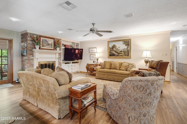 living area with ceiling fan, a textured ceiling, visible vents, crown molding, and light wood-style flooring