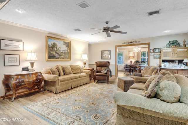 living area featuring crown molding, a textured ceiling, ceiling fan with notable chandelier, light wood-type flooring, and visible vents