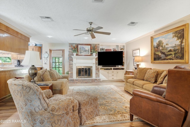 living area with visible vents, ornamental molding, a brick fireplace, ceiling fan, and light wood-style flooring