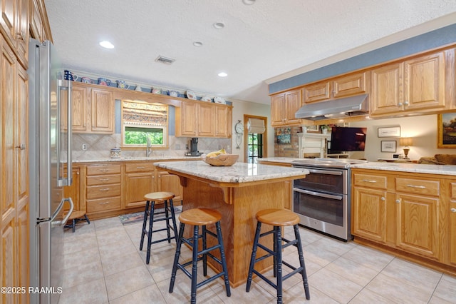 kitchen featuring visible vents, a breakfast bar area, a center island, under cabinet range hood, and stainless steel appliances