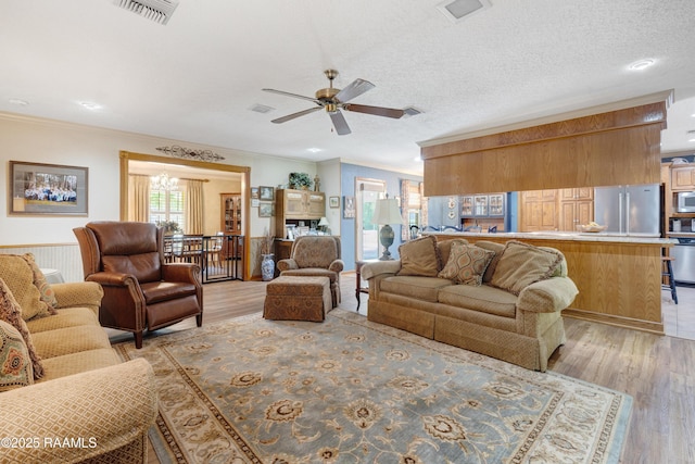 living room with visible vents, light wood finished floors, crown molding, and ceiling fan with notable chandelier